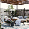 竹のソファと丸テーブルのあるパーゴラの下のウッドデッキの屋外リビング
